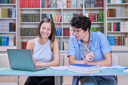 Young male and female students sitting at desk in college library, with books, notebooks, studying, preparing for exams. Knowledge, education, youth, college university concept