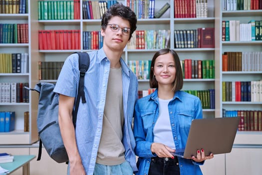 Portrait of two college students, guy and girl, smiling looking at camera inside library. Knowledge, education, youth, college university concept