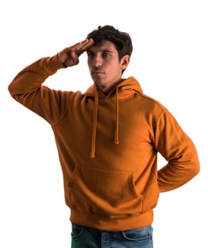 A man in an orange hoodie is standing at attention, with hand on his forehead, in studio shot, looking at camera