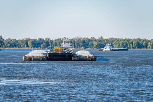 Two large tug boats pushing rows of barges with grain and petroleum products down the Upper Mississippi river