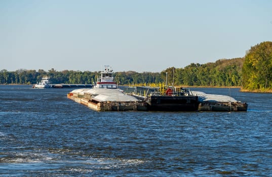 Two large tug boats pushing rows of barges with grain and petroleum products down the Upper Mississippi river