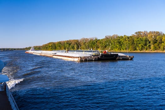 Two large tug boats pushing rows of barges with grain and petroleum products down the Upper Mississippi river