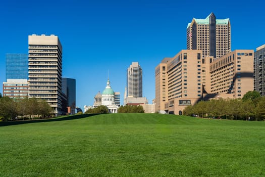 View across green lawn of Gateway Arch National Park with other office buildings in downtown cityscape