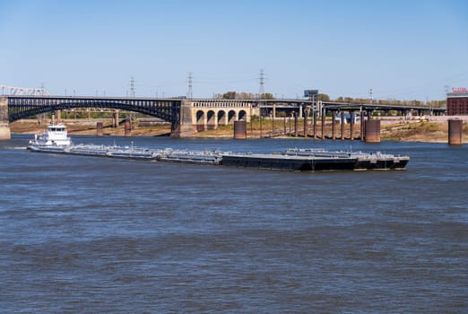 Powerful pusher tugboat with barges of petroleum products under Eads Bridge in St Louis, Missouri