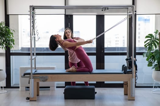Asian woman doing pilates with trainer on cadillac reformer