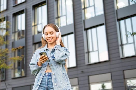 Young fair haired woman in headphones selects music on smart phone.