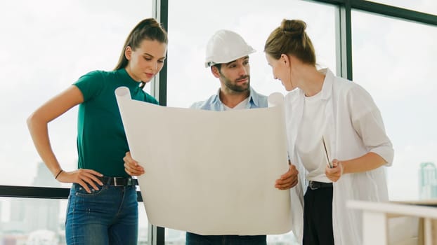 Professional architect engineer team talking, sharing, brainstorming about design while manager hold at project plan. Young architect holding plan while manager listen and point at plan. Tracery