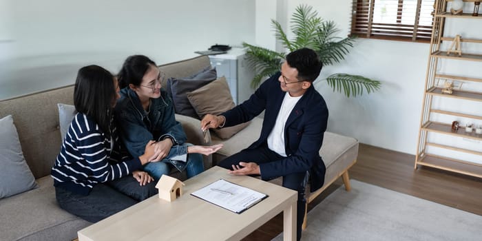 Happy real state agent giving new house key to a young lesbian LGBTIQA couple.