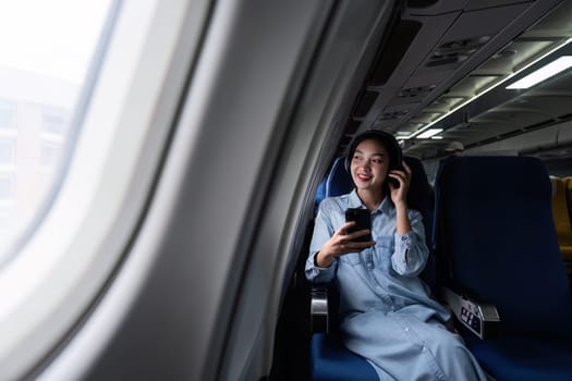 Asian people female person onboard, airplane window, using mobile and headphone while on the plane.