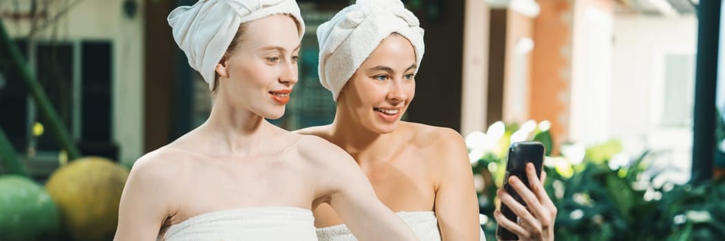 Couple of young beautiful women with beautiful skin in white towel taking a photo together at outdoor surrounded by peaceful natural environment. Beauty and healthy spa concept. Tranquility.