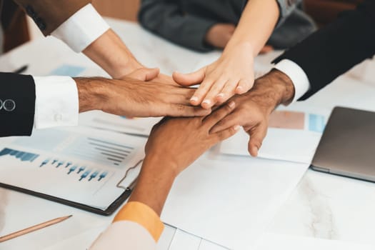 Top view of corporate diverse businesspeople putting hands together on meeting table with document scatter around at business meeting room. Represented unity, cooperation, collaboration. Ornamented.