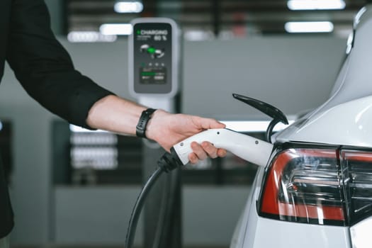 Young man travel with EV electric car to shopping center parking lot charging in downtown city showing urban sustainability lifestyle by green clean rechargeable energy of electric vehicle innards