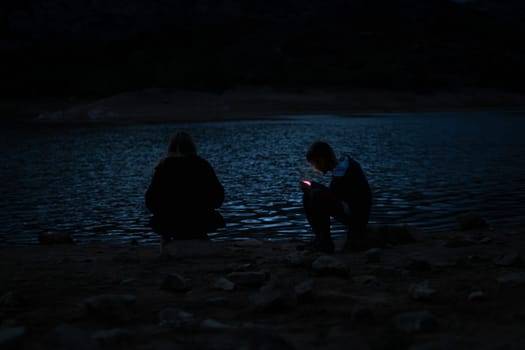 boy and girl sitting near the lake at the campsite in the evening, family vacation concept. High quality photo