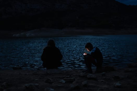 boy and girl sitting near the lake at the campsite in the evening, family vacation concept. High quality photo