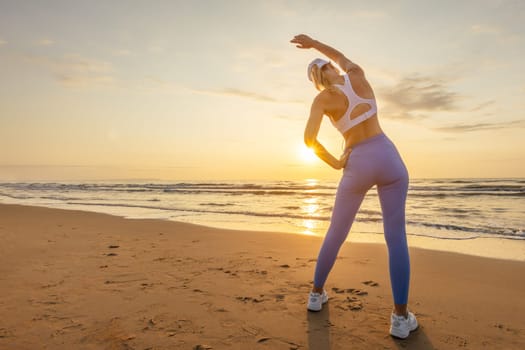 a thin girl in blue tights and a white top stands against the backdrop of the sea at dawn doing exercises, the concept of a healthy lifestyle. High quality photo