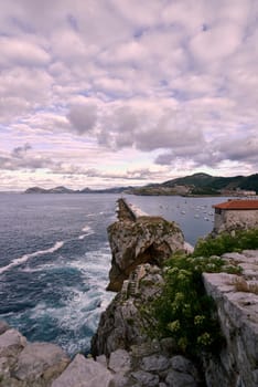 Castro Urdiales breakwater and fishing harbour in Spain. Moving sun and clouds, small boats, rocks, calm sea, mountains and vegetation.
