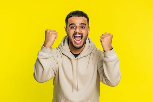 Happy joyful Indian man celebrating success victory, winning birthday, lottery jackpot goal achievement play game good positive news, triumph. Young Arabian guy isolated on yellow studio background