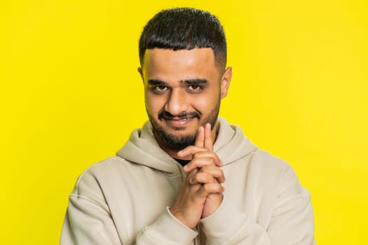 Sneaky cunning Indian young man with tricky face gesticulating and scheming evil plan thinking over devious villain idea, cheats, jokes, pranks. Arabian Hindu guy isolated on yellow background indoors