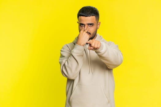 I am watching you. Confident attentive Arab man pointing at her eyes and camera, show I am watching you gesture spying on someone. Disappointed Indian Hindu guy isolated on yellow studio background