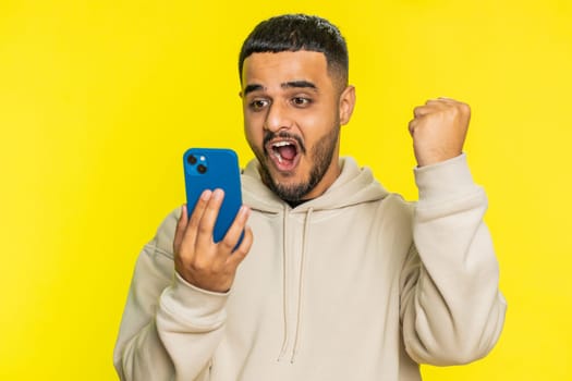 Happy excited Indian Hindu man guy use smartphone typing browsing shouting say wow yes found out great big win good news lottery goal achievement celebrating success, winning play game on yellow