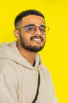 Cheerful lovely happy young Indian man smiling friendly glad expression looking at camera dreaming resting relaxation feel satisfied good news. Arabian bearded guy isolated on yellow studio background