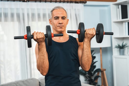 Athletic and sporty senior man engaging in body workout routine with lifting dumbbell at home as concept of healthy fit body with body weight lifestyle after retirement. Clout