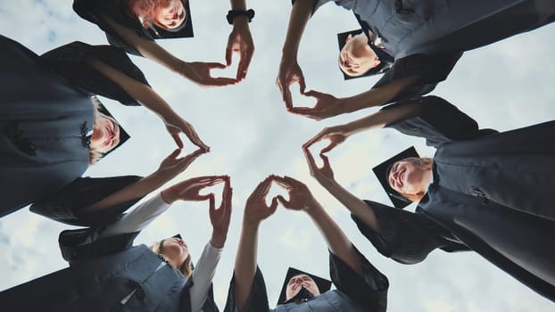 A group of college graduates stand in a circle and make hearts out of their palms