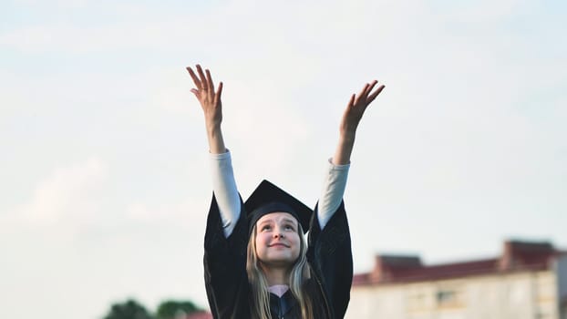 Joyful girl student graduates with her hands in the air