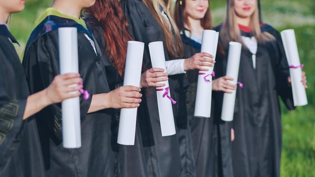 Scrolls of diplomas in the hands of a group of graduates