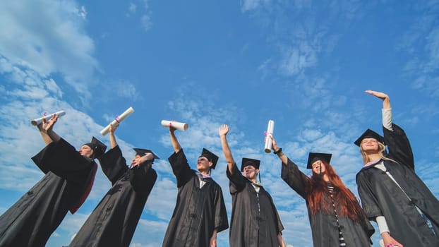 Cheerful graduates pose with raised diplomas on a sunny day