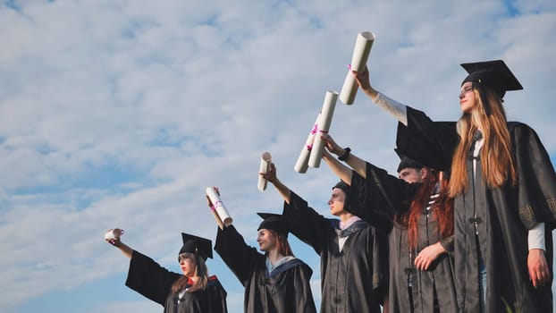 Cheerful graduates pose with raised diplomas on a sunny day