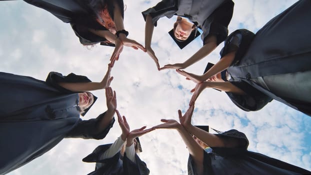 Students graduating from the college make a heart out of their hands