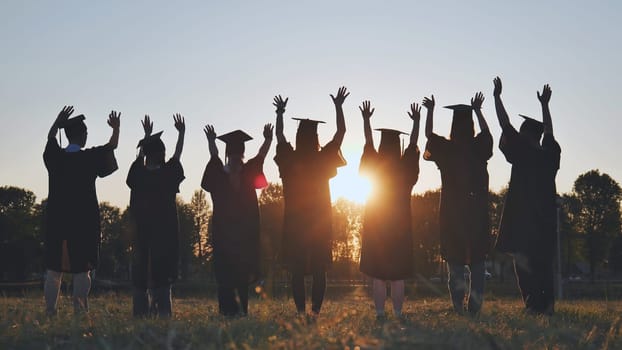 College graduates in robes waving at sunset