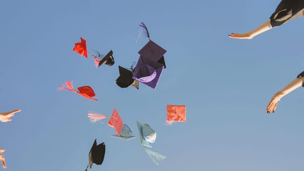 Graduates tossing multicolored hats against a blue sky
