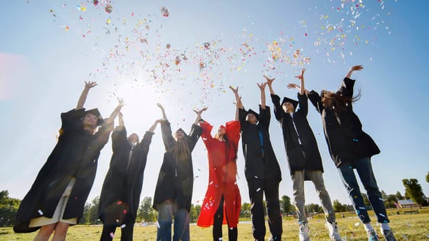 Happy college graduates throw colorful confetti against the rays of sunshine