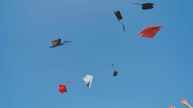 Graduates tossing multicolored hats against a blue sky
