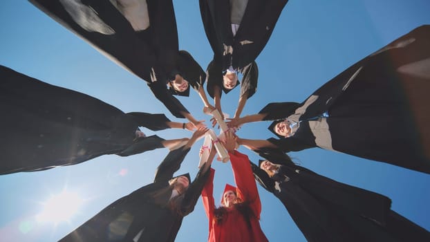 College graduates join hands with diplomas standing in a circle