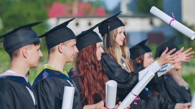 Cheerful graduates pose with raised diplomas on a sunny day