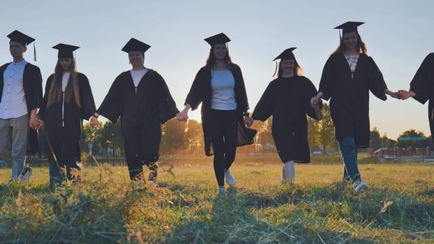 College graduates hold hands at sunset to meet the future and the sun