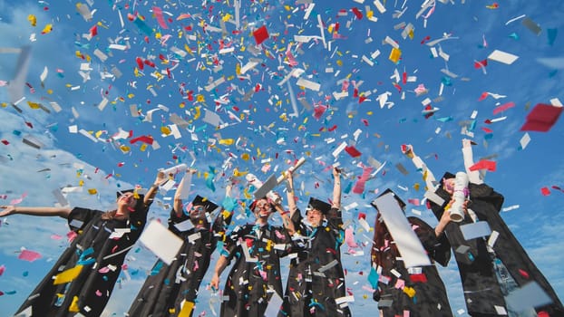 Graduates throw colorful confetti against a blue sky