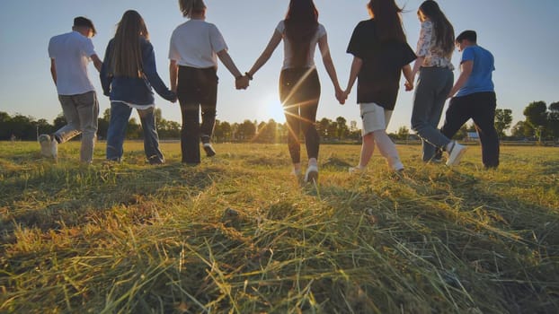 Friends at sunset holding hands walking towards the sun