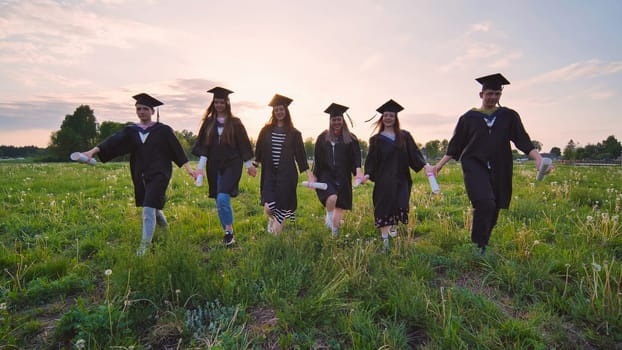 Six graduates in robes walk against the backdrop of the sunset