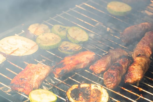 Grilling meat rolls called mici or mititei with vegetables on char barbecue. Charcoal grill with burning fire