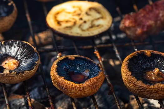 Grilling meat rolls called mici or mititei with vegetables on char barbecue. Charcoal grill with burning fire