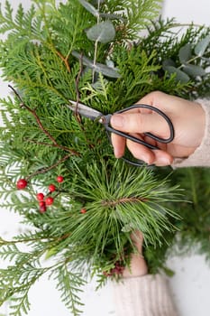 The concept of preparation for Christmas and New Year, hobby, handwork. The process of making a Christmas wreath from chopped branches of various conifers