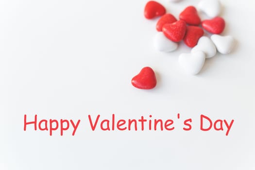 Valentine's day pattern background flat lay top view of red and white heart shaped candies scattered on white background. Happy valentine's day lettering