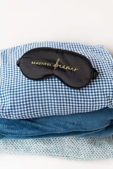 A sleeping mask with the inscription beautiful dreamer lies on bed linen of different shades of blue, blue, white and different structures, which are stacked on top of each other