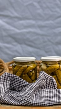 Glass jars with pickled red bell peppers and pickled cucumbers (pickles) isolated. Jars with variety of pickled vegetables. Preserved food concept in a rustic composition.