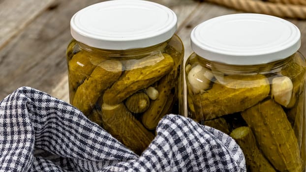 Glass jars with pickled red bell peppers and pickled cucumbers (pickles) isolated. Jars with variety of pickled vegetables. Preserved food concept in a rustic composition.