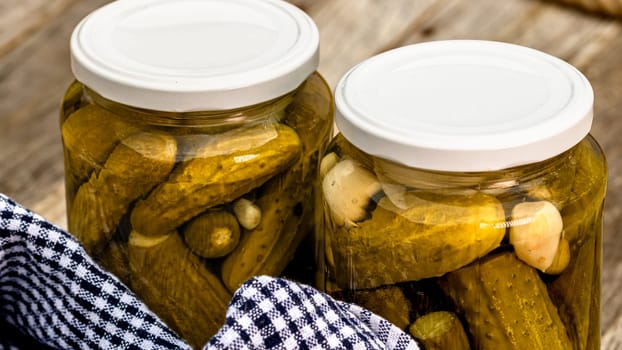 Glass jars with pickled red bell peppers and pickled cucumbers (pickles) isolated. Jars with variety of pickled vegetables. Preserved food concept in a rustic composition.